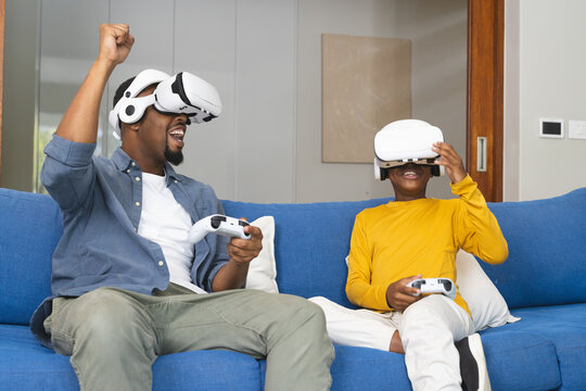 African American father and son playing video games with VR headsets at home