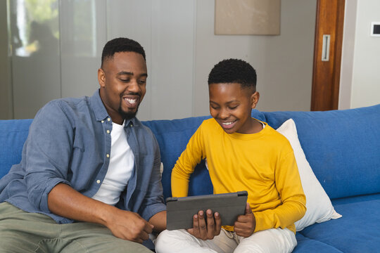 Father and son using tablet on couch, enjoying quality time together at home