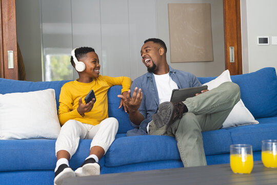 African American father and son enjoying music and conversation on living room sofa