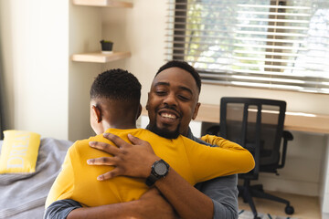 African American father and son hugging in modern room, with desk, cozy bed and small plant