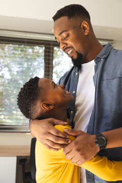 African American father hugging son at home, both smiling and looking happy