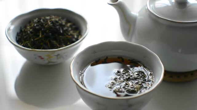 Una taza de t&eacute; con tetera y hojas de t&eacute; sobre una mesa blanca.