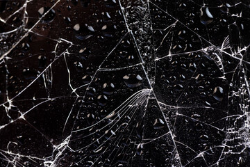 water covered glass with a lot of damage on a black background, wet thin glass broken into many...
