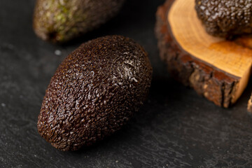 wet whole black avocado fruits of small size on a black slate, ripe avocado fruit in drops of water, closeup