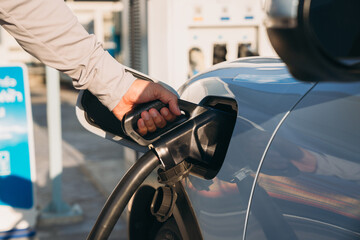 Close-up of a hand plugging an electric vehicle charger into a charging station, clean energy and...
