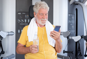 Portrait of smiling senior Man Hydrating After Workout in Gym, towel around his neck and earphones....
