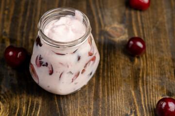 fresh yogurt with cherry flavor and berry slices, jar with cherry yogurt with fresh red cherries close up, side view