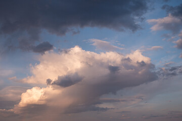 Fototapeta premium Cloudy sky with sunlit cumulus clouds and dark shadows during sunset. A natural sky view symbolizing change, peace, and light from above. 