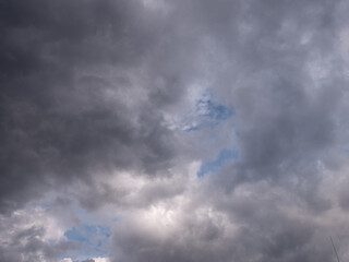 Dark clouds covering the sky with small patches of blue. A natural weather scene that suggests a break in the storm, often symbolizing hope and spiritual awakening.
