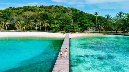 Couple walking hand in hand along a tropical dock over turquoise waters on a sunny day