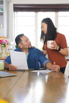 Mature couple discussing finances at kitchen table, holding documents and coffee