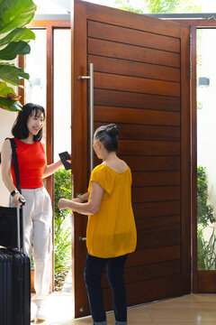 Asian family arriving at home entrance through front door, with rolling suitcase and smartphone