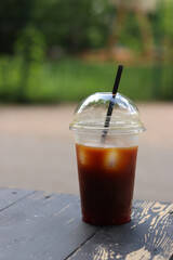 Bumble coffee in disposable cup on wooden table, close-up. Iced coffee outdoors with blurred park in background. Cold coffee in plastic disposable cup with straw. Takeaway drink
