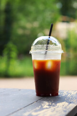 Bumble coffee in disposable cup on wooden table, close-up. Iced coffee outdoors with blurred park in background. Cold coffee in plastic disposable cup with straw. Takeaway drink