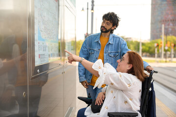 Woman in wheelchair and friend consulting a tram map at station - wheelchair and disability concept