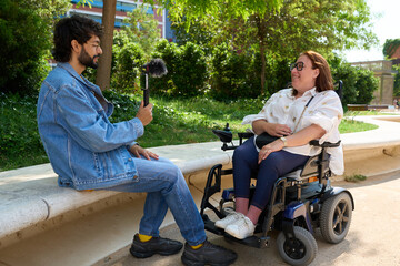 Journalist interviewing disabled woman in wheelchair in park - wheelchair and disability concept