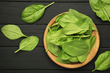 Spinach leaves in a wooden plate on black wooden background.