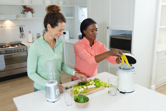 Diverse female friends chopping and composting scraps at kitchen island, with compost pail - Powered by Adobe