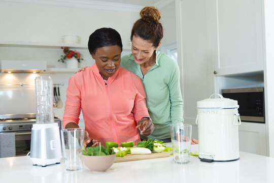 Slicing green vegetables on cutting board, diverse female friends preparing meal in home kitchen