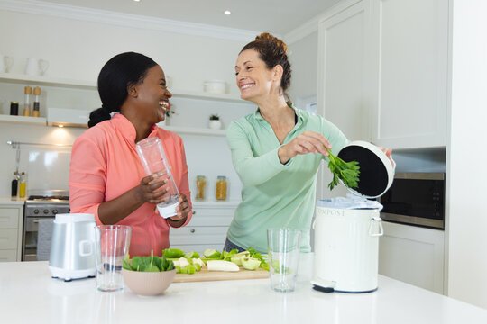 Diverse female friends chopping greens and composting in kitchen, with blender and compost bin