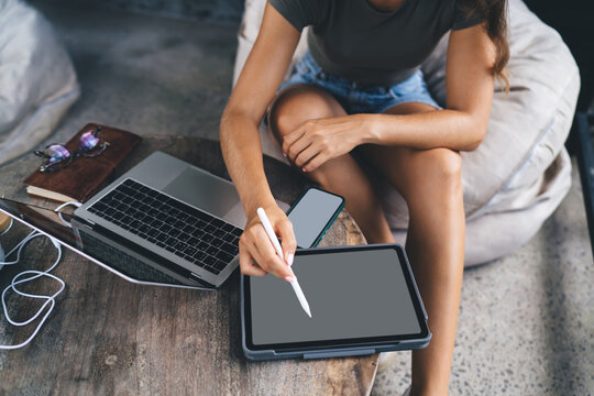 Top view of freelancer working from tablet with stylus, sitting cross-legged near laptop and smartphone, managing business tasks in modern mobile workspace - Powered by Adobe