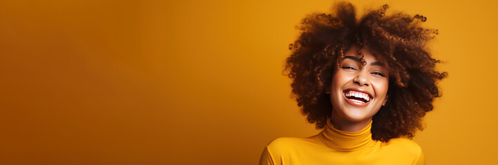 Happy laughing African American young woman on a yellow background. Photo with copy space.
