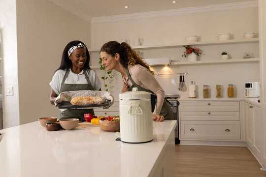 Baking Diverse female friends making fresh bread at kitchen island, with vegetables and oven mitts