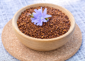 Ground chicory root in a wooden cup and chicory flowers on a rustic wooden background. Alternative medicine. Healthy drinks. chicory drink