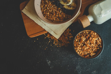 Top view of oatmeal bowl with banana, chia seeds, dried cherries, and granola, placed on wooden...