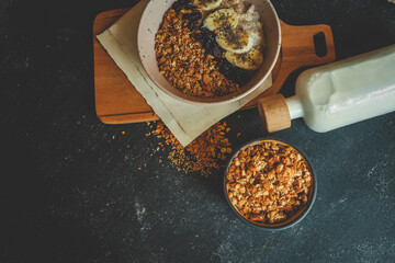 Top view of oatmeal bowl with banana, chia seeds, dried cherries, and granola, placed on wooden...