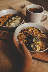 Cozy morning scene with two ceramic bowls of oatmeal topped with banana slices, granola, and chia seeds, next to a mug of tea and a waffle towel