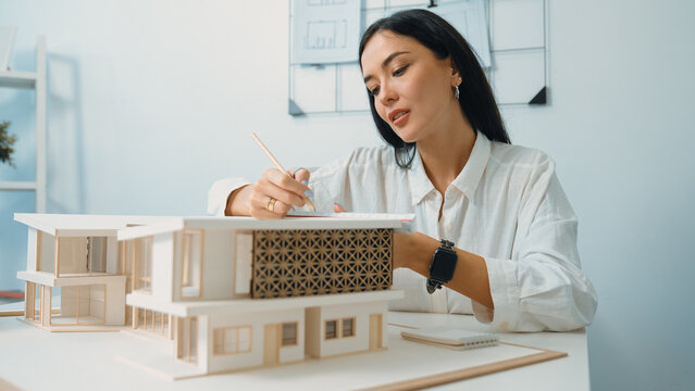 Closeup portrait image of professional young beautiful engineer architect using triangular scale measures house model with focusing at modern office. Business creative design concept. Immaculate.
