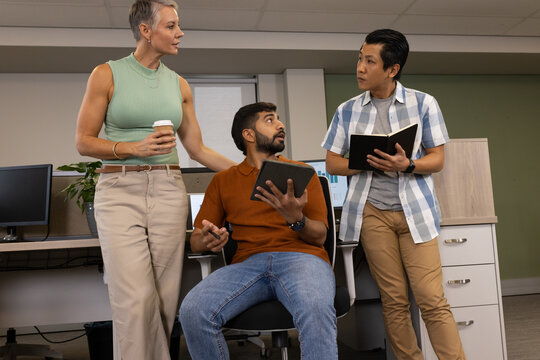 Diverse coworkers discussing project in office cubicle, with digital tablet and coffee cup