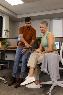 Pointing Diverse coworkers reviewing tablet data in office cubicle, with laptop and plant