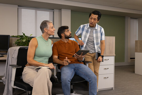 Diverse coworkers collaborating around workstation in office, with tablet and notebook
