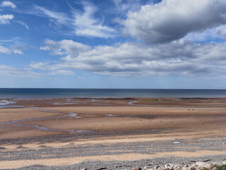 Coastal view with blue sky, scattered clouds, and tranquil sandy beach meeting the sea