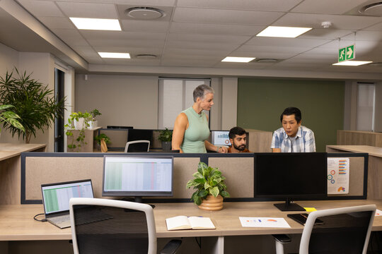 Collaborating Diverse coworkers reviewing printed charts in open-plan office, with dual monitors