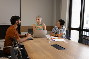 Discussing Diverse coworkers collaborating around table in conference room, with laptop, documents