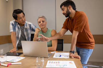 Leaning Diverse coworkers discussing data at table in meeting room, with laptop and charts