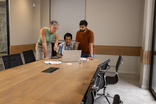 Collaborating Diverse coworkers leaning over laptop at meeting table with documents and smartphone