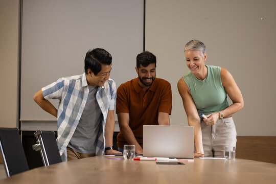 Collaborating diverse coworkers reviewing slides on laptop at conference table, with notebooks pens