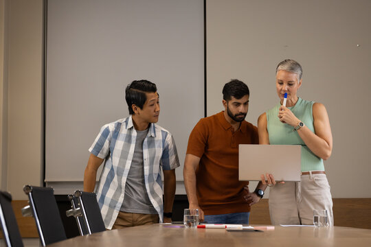 Reviewing Diverse coworkers leaning over laptop in boardroom, with colorful markers and documents