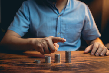Hand of a Person Pointing at Stacked Coins on a Wooden Table in a Dimly Lit Environment