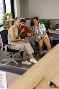 Collaborating Diverse coworkers analyzing data on laptop in open-plan office, with red coffee mug