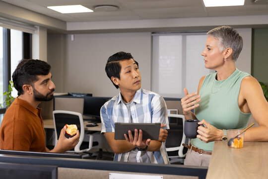 Talking Diverse coworkers standing at office counter, with apple tablet coffee mug and fruit cup