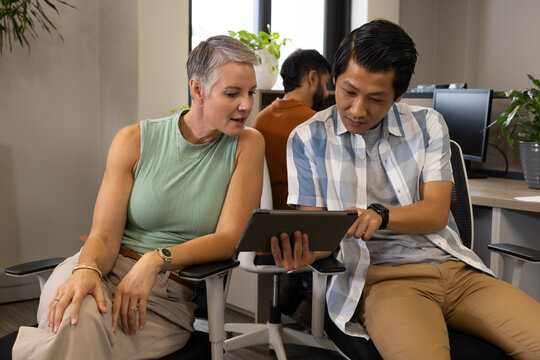 Collaborating Diverse coworkers reviewing tablet in open-plan office, with chairs and plants