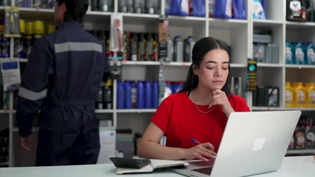 Young saleswoman managing orders and calculating prices in an auto parts store