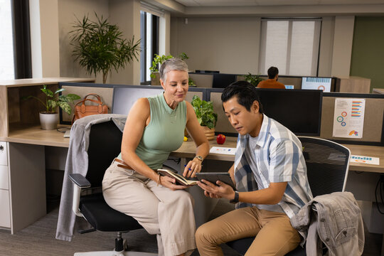 Diverse coworkers collaborating in modern open-plan office, with notebook and tablet