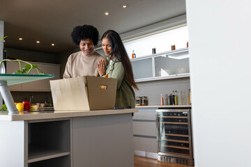 Smiling Diverse couple unpacking groceries at kitchen island, with cardboard box and bell peppers