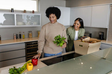 Unpacking diverse couple sorting vegetables at kitchen island, with bell peppers and leafy greens